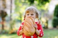 Little toddler girl holding big loaf of bread. Funny happy child biting and eating healthy bread, outdoors. Hungry kid. Royalty Free Stock Photo