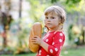 Little toddler girl holding big loaf of bread. Funny happy child biting and eating healthy bread, outdoors. Hungry kid. Royalty Free Stock Photo