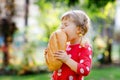 Little toddler girl holding big loaf of bread. Funny happy child biting and eating healthy bread, outdoors. Hungry kid. Royalty Free Stock Photo