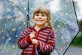 Little toddler girl playing with big umbrella on rainy day. Happy positive child running through rain, puddles Royalty Free Stock Photo