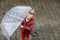 Little toddler girl playing with big umbrella on rainy day. Happy positive child running through rain, puddles