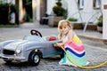 Little toddler girl playing with big vintage toy car and having fun outdoors in summer. Cute child refuel car with water Royalty Free Stock Photo