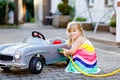 Little toddler girl playing with big vintage toy car and having fun outdoors in summer. Cute child refuel car with water Royalty Free Stock Photo