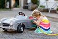 Little toddler girl playing with big vintage toy car and having fun outdoors in summer. Cute child refuel car with water Royalty Free Stock Photo