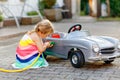 Little toddler girl playing with big vintage toy car and having fun outdoors in summer. Cute child refuel car with water Royalty Free Stock Photo