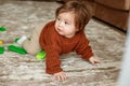 Cute baby girl crawling on floor at home, playing with colored building blocks. Brown sweater Royalty Free Stock Photo