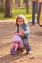 Little toddler girl riding a small pink bike in the sunlit park Royalty Free Stock Photo