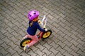 Little toddler girl running with balance bike on summer day. Happy child driving, biking with bicycle, outdoor activity