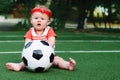 Little toddler girl in sport shirt and red hair band playing with a soccer ball at football field outdoors in summer day Royalty Free Stock Photo