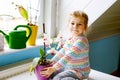 Little toddler girl watering flowers and orchid plants on window at home. Cute child helping, domestic life. Happy Royalty Free Stock Photo
