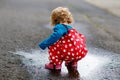 Little toddler girl wearing rain boots and trousers and walking during sleet, rain on cold day. Baby child having fun Royalty Free Stock Photo