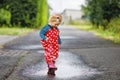 Little toddler girl wearing rain boots and trousers and walking during sleet, rain on cold day. Baby child having fun Royalty Free Stock Photo