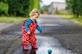 Little toddler girl wearing rain boots and trousers and walking during sleet, rain on cold day. Baby child having fun Royalty Free Stock Photo