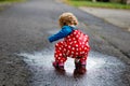 Little toddler girl wearing rain boots and trousers and walking during sleet, rain on cold day. Baby child having fun Royalty Free Stock Photo