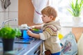 Little toddler helping in kitchen with washing dishes Royalty Free Stock Photo