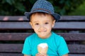 Little toddler kid in blue hat eating ice-cream in waffle cone outdoors in summer or autumn weekend. Leisure concept Royalty Free Stock Photo