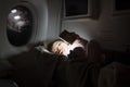 Little toddler lies in special baby bassinet on a plane in the dark and playing with a flashlight