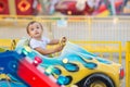 Little toddler in theme park: a boy in white shirt riding little car on merry go round, bright amusements in background Royalty Free Stock Photo