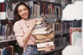 A little too much. Brunette girl in casual clothes having good time in the library full of books Royalty Free Stock Photo