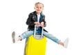 Little tourist with extended legs sitting on yellow wheel suitcase