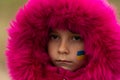 A little Ukrainian refugee girl with a Ukrainian flag painted on her cheek is sad about her lost home. Stop the war in