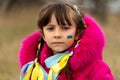 A little Ukrainian refugee girl with a Ukrainian flag painted on her cheek is sad about her lost home. Stop the war in