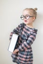 Little unhappy girl with round glasses holding heavy book in hand. Little teacher