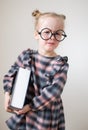 Little unhappy girl with round glasses holding heavy book in hand. Little teacher