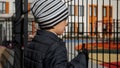 Little upset boy looking through metal fence on modern school and playground. Concept of poverty, immigration, bullying Royalty Free Stock Photo