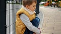 Little upset boy sitting next to metal fence feeling unhappy and lonely. Child depression, problems with bullying, victim in Royalty Free Stock Photo