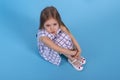 A  little upset girl with long blonde hair sits on blue background in studio, top view Royalty Free Stock Photo