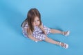 A  little upset girl with long blonde hair sits on blue background in studio, top view Royalty Free Stock Photo