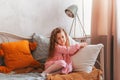 Little vintage girl sits on a bed in a children`s bedroom and dreams