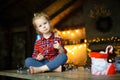 Little white blonde girl sitting on a wooden table in the living room of the Chalet, decorated for Christmas tree and garlands wit Royalty Free Stock Photo