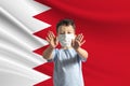 Little white boy in a protective mask on the background of the flag of Bahrain. Makes a stop sign with his hands, stay at home