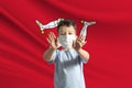 Little white boy in a protective mask on the background of the flag of Isle of Man. Makes a stop sign with his hands, stay at home