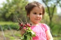 Little white girl in a pink t-shirt holding an armful of red radishes with green leaves in her hands on a blurred garden