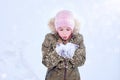 A little winter girl in the outdoors on a white background in a winter hat and jacket blows snow off her mittened hands Royalty Free Stock Photo