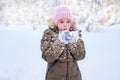 A little winter girl in the outdoors on a white background in a winter hat and jacket blows snow off her mittened hands Royalty Free Stock Photo