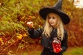 A little witch collects wild berries for a potion, holds a bottle in the form of a skull with a red liquid in her hands Royalty Free Stock Photo