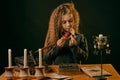 Little witch dressed in dark clothes sitting at the table against a black smoky background. There are magic wand, books Royalty Free Stock Photo