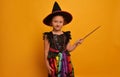 Little witch girl with magic wand or magic stick standing on a yellow background. Child girl wearing Halloween costume. Royalty Free Stock Photo