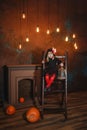 A little witch sits on the stairs with a lantern, smiling Royalty Free Stock Photo