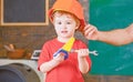 Little worker helping daddy in workshop. Kid playing with toy handsaw and spanner. Father holding protective helmet on Royalty Free Stock Photo