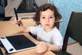 Little 2 3 year old baby girl in white clothers draws at the home computer in graphics drawing tablet. The child is holding a pen Royalty Free Stock Photo