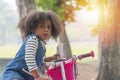 Black girl want learn ride bicycle eating chocolate in her mouth while standing in the park with tree. Mixed