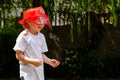 A little young school age girl wearing a red firefighter toy helmet being sprayed with water, outdoors, child playing outside Royalty Free Stock Photo