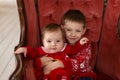 Litttle brother hugs his little sister in red retro chair near Christmas Tree. Enjoying a love hug, people`s holidays.
