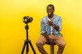 Live blog. Portrait of positive friendly happy man smiling at his professional dslr camera. isolated on yellow background Royalty Free Stock Photo