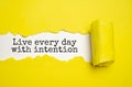 Live every day with intention. Words written under torn paper. Motivation concept text